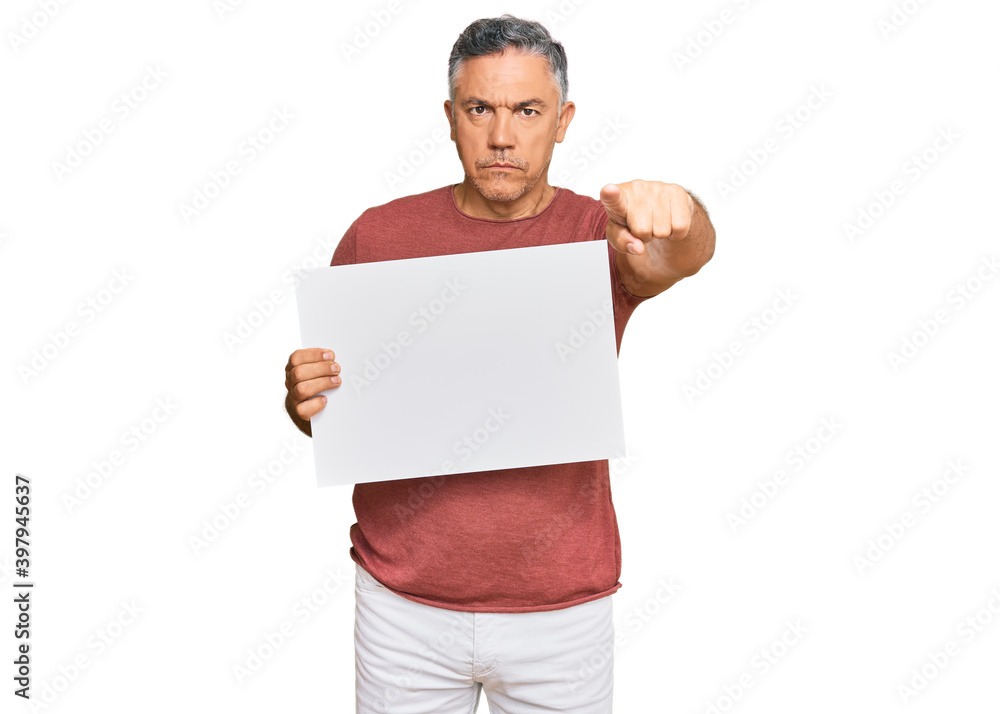 Handsome middle age man holding blank empty banner pointing with finger to the camera and to you, confident gesture looking serious Handsome middle age man holding blank empty banner pointing with finger to the camera and to you, confident gesture looking serious