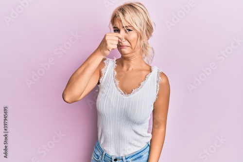 Young blonde girl wearing casual clothes smelling something stinky and disgusting  intolerable smell  holding breath with fingers on nose. bad smell