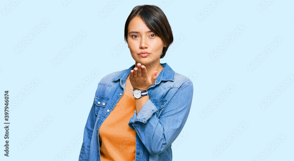 Young beautiful hispanic woman with short hair wearing casual denim jacket looking at the camera blowing a kiss with hand on air being lovely and sexy. love expression. Young beautiful hispanic woman with short hair wearing casual denim jacket looking at the camera blowing a kiss with hand on air being lovely and sexy. love expression.