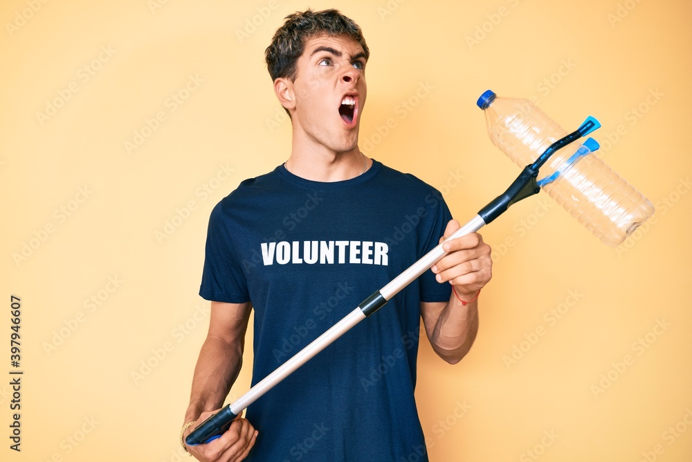 Young handsome man recycling plastic bottle holding litter pick up tool angry and mad screaming frustrated and furious, shouting with anger. rage and aggressive concept. Young handsome man recycling plastic bottle holding litter pick up tool angry and mad screaming frustrated and furious, shouting with anger. rage and aggressive concept.