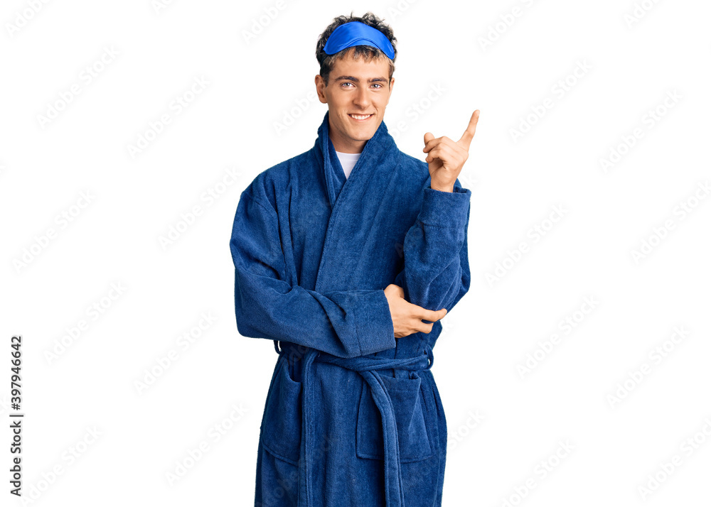 Young handsome man wearing sleep mask and bathrobe smiling happy pointing with hand and finger to the side Young handsome man wearing sleep mask and bathrobe smiling happy pointing with hand and finger to the side
