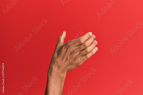 Bilde på lerret Hand of hispanic man over red isolated background holding invisible object, empt