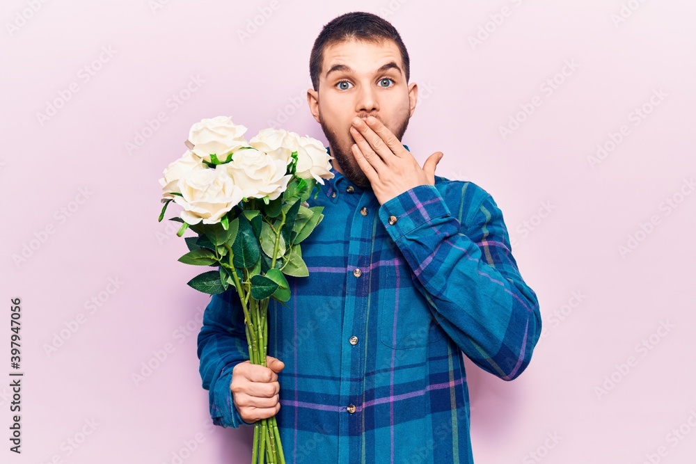Young handsome man holding bouquet of flowers covering mouth with hand, shocked and afraid for mistake. surprised expression Young handsome man holding bouquet of flowers covering mouth with hand, shocked and afraid for mistake. surprised expression