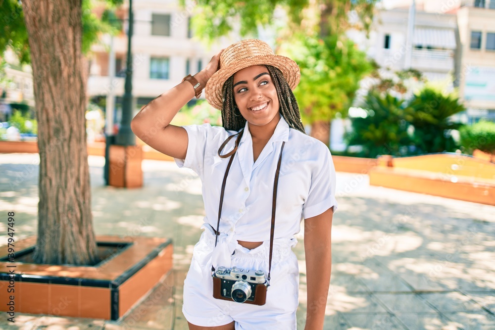 Young african american woman with braids smiling happy wearing vintage camera outdoors on a sunny day of summer