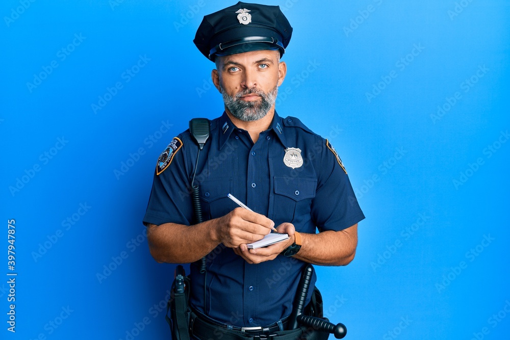 Middle age handsome man wearing police uniform writing traffic fine relaxed with serious expression on face. simple and natural looking at the camera. Middle age handsome man wearing police uniform writing traffic fine relaxed with serious expression on face. simple and natural looking at the camera.