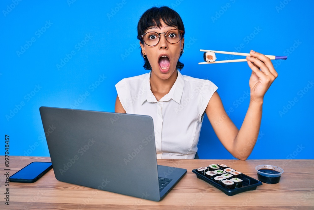 Beautiful brunettte woman working at the office eating sushi afraid and shocked with surprise and amazed expression, fear and excited face. Beautiful brunettte woman working at the office eating sushi afraid and shocked with surprise and amazed expression, fear and excited face.