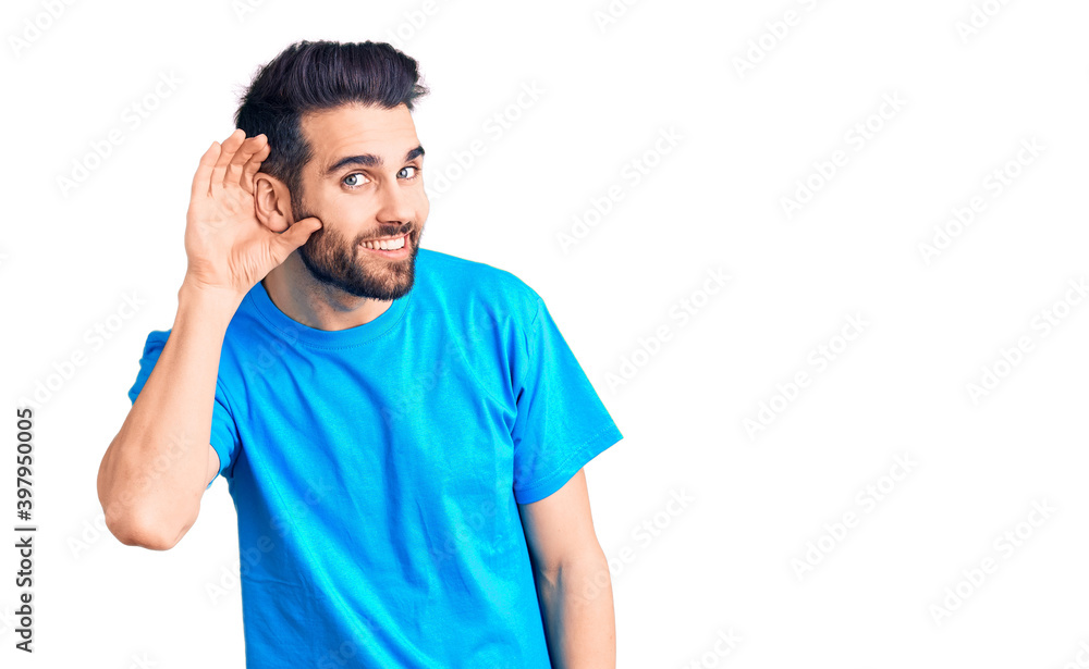 Young handsome man with beard wearing casual t-shirt smiling with hand over ear listening an hearing to rumor or gossip. deafness concept. Young handsome man with beard wearing casual t-shirt smiling with hand over ear listening an hearing to rumor or gossip. deafness concept.