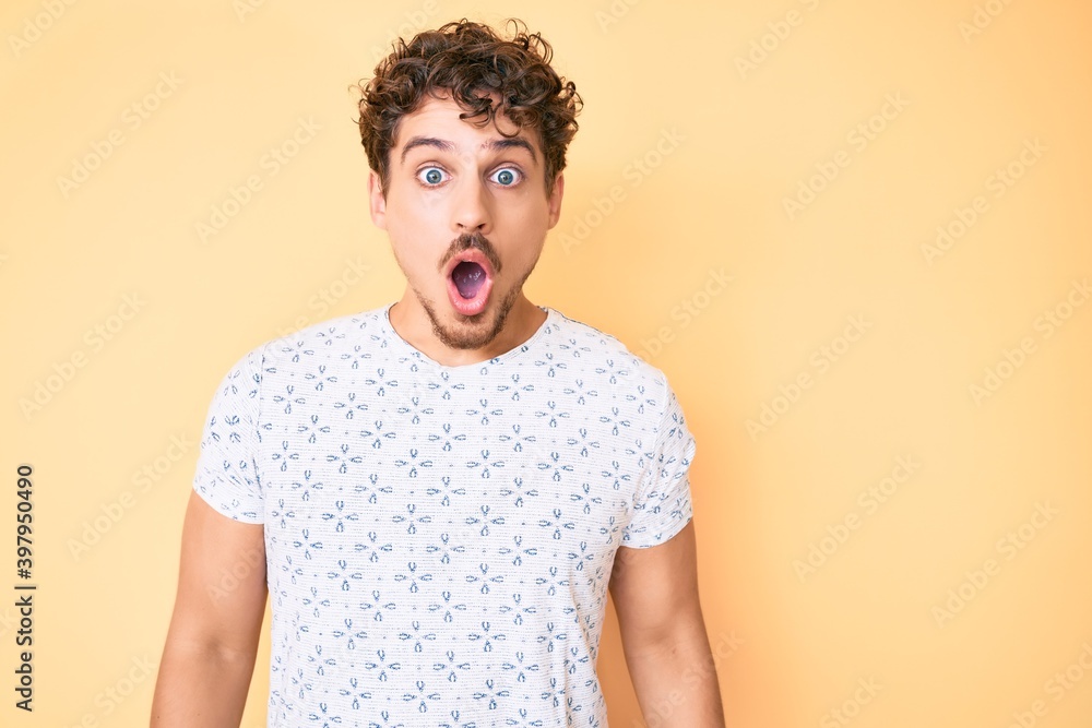 Young caucasian man with curly hair wearing casual clothes scared and amazed with open mouth for surprise, disbelief face Young caucasian man with curly hair wearing casual clothes scared and amazed with open mouth for surprise, disbelief face