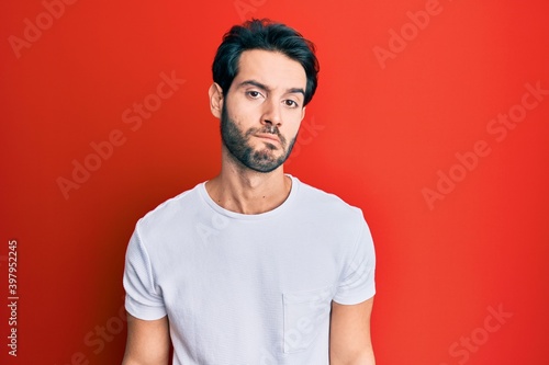 Young hispanic man wearing casual white tshirt looking sleepy and tired, exhausted for fatigue and hangover, lazy eyes in the morning.