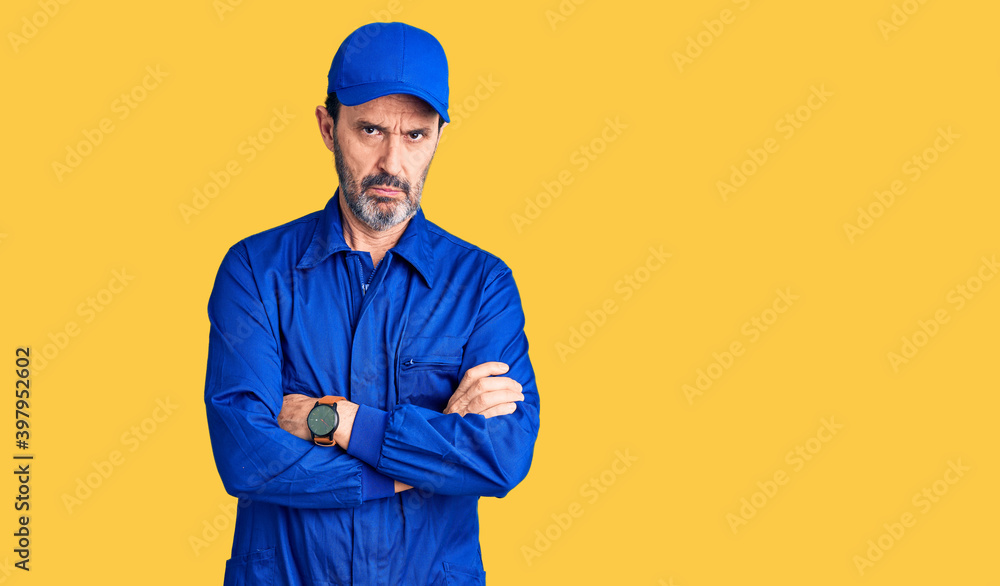 Middle age handsome man wearing mechanic uniform skeptic and nervous, disapproving expression on face with crossed arms. negative person.