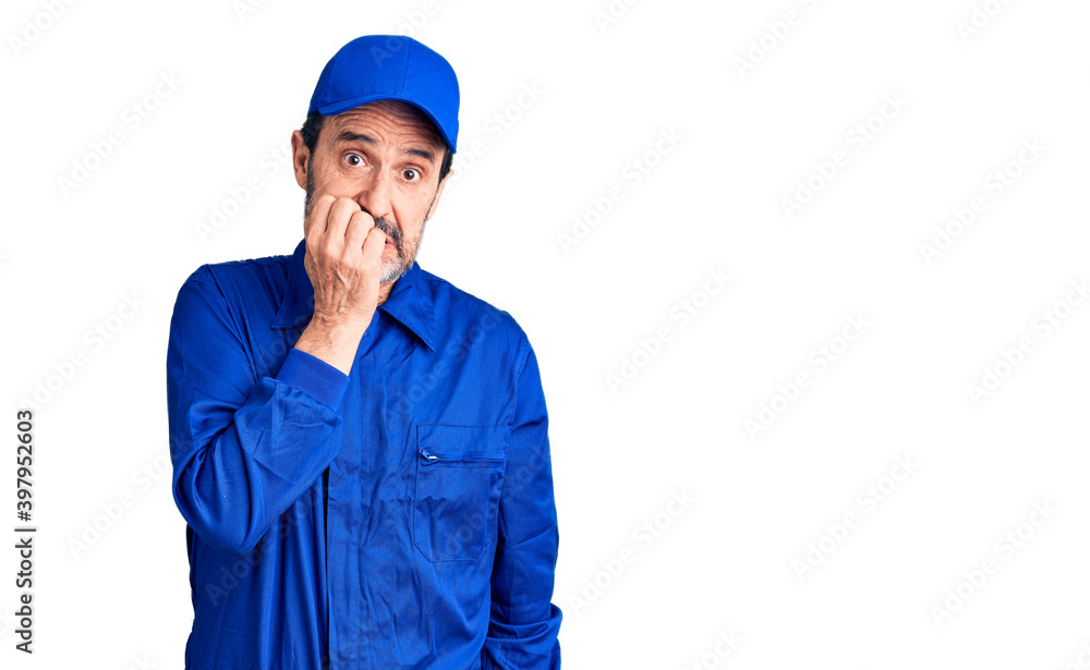 Middle age handsome man wearing mechanic uniform looking stressed and nervous with hands on mouth biting nails. anxiety problem.