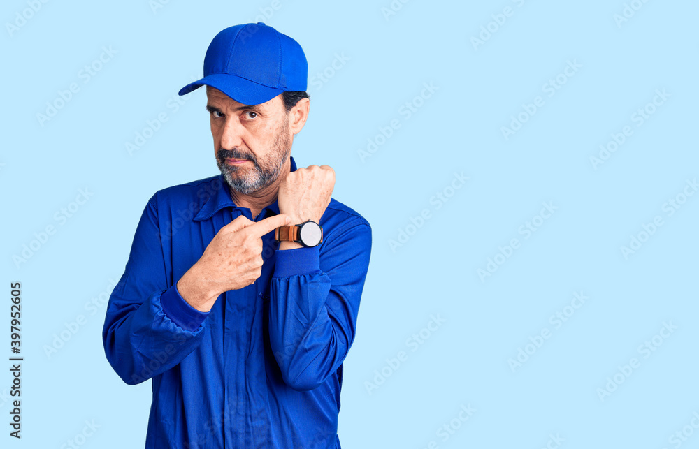 Middle age handsome man wearing mechanic uniform in hurry pointing to watch time, impatience, looking at the camera with relaxed expression