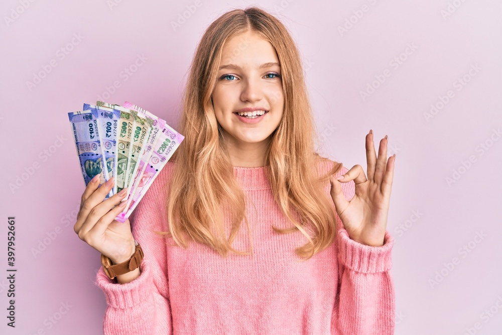 Beautiful young caucasian girl holding indian rupee banknotes doing ok sign with fingers, smiling friendly gesturing excellent symbol Beautiful young caucasian girl holding indian rupee banknotes doing ok sign with fingers, smiling friendly gesturing excellent symbol
