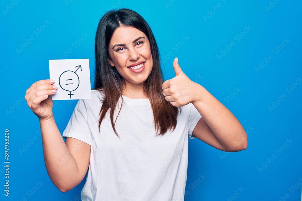 Young beautiful woman asking for sex discrimination holding paper with gender equality concept smiling happy and positive, thumb up doing excellent and approval sign Young beautiful woman asking for sex discrimination holding paper with gender equality concept smiling happy and positive, thumb up doing excellent and approval sign