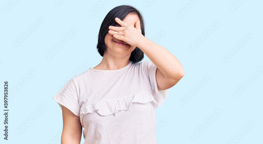 Brunette woman with down syndrome wearing casual white tshirt smiling and laughing with hand on face covering eyes for surprise. blind concept. Brunette woman with down syndrome wearing casual white tshirt smiling and laughing with hand on face covering eyes for surprise. blind concept.