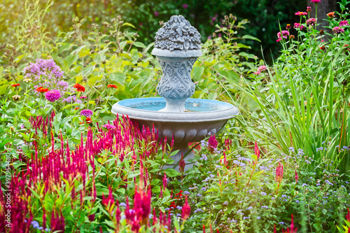 Water fountain in a backyard garden filled with summer flowers in bloom - celosia, ageratum and zinnia
