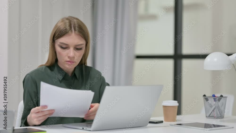 Young Woman Reading Documents while working on Laptop Young Woman Reading Documents while working on Laptop