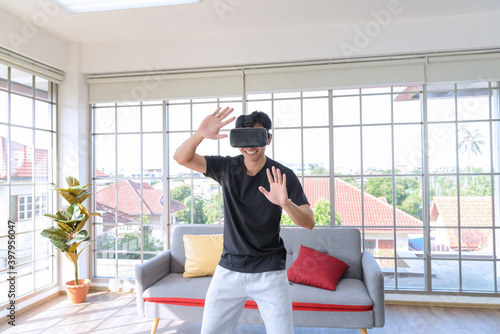 Young Asian man getting experience with VR virtual reality headset or 3D glasses in living room at home. technology, gaming, entertainment concept