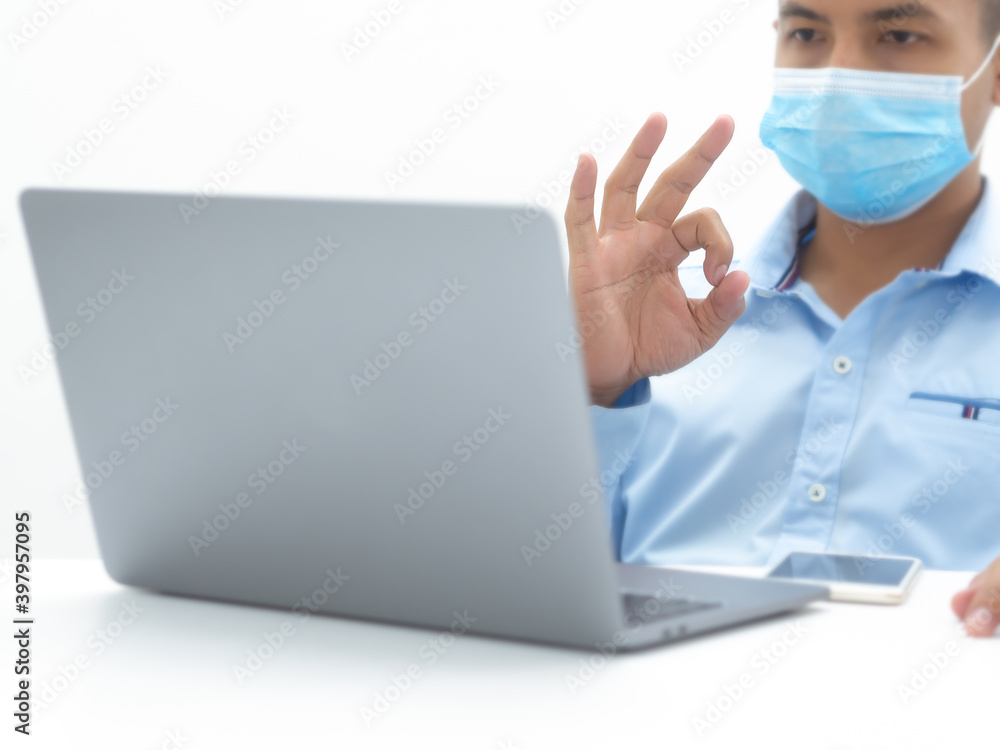 Businessman doing ok hand Raise your right hand to chat online Through computer Wearing a blue long sleeve shirt Wear a mask, concept covid-19, covid economy, communicate online. Businessman doing ok hand Raise your right hand to chat online Through computer Wearing a blue long sleeve shirt Wear a mask, concept covid-19, covid economy, communicate online.