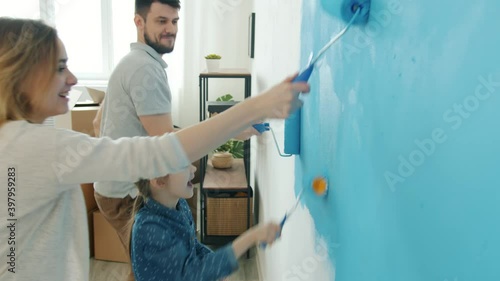 Playful people mother father and child are painting wall at home and dancing laughing having fun enjoying apartment renovation. Family and accommodation concept.