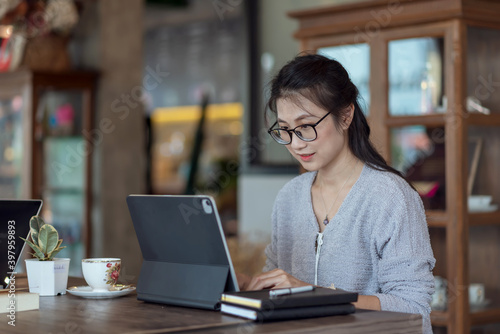 Happy young Asian woman working in a coffee shop with a digital tablet.