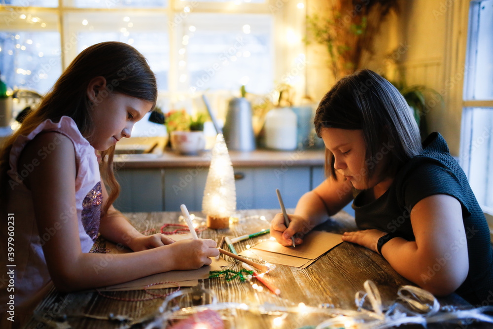 Fototapeta premium Caucasian girls children draw and write letters at the table against the background of lights
