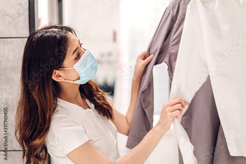 Young beautiful asian woman in quarantine for coronavirus wearing surgical mask face protection with social distancing shopping and choosing clothes at store.covid19 and new normal concept