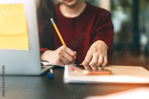Young adult women hand writing note for study and work online at cafe table with laptop.