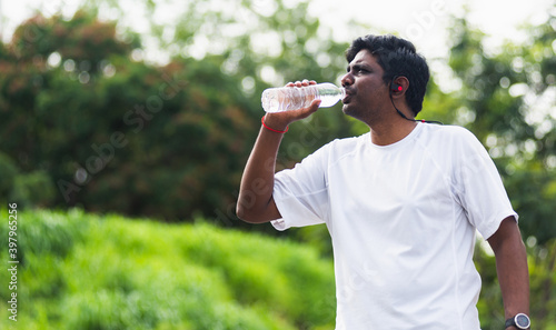 Close up Asian young sport runner black man wear athlete headphones he drinking water from a bottle after running at the outdoor street health park, healthy exercise workout concept