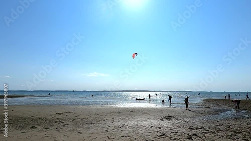 A beach scene in the summer with people walking and kitesurfers in the water