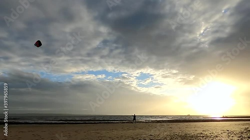 A man flying a power kite quickly through the air in figures of 8 on a beach during sunset photo