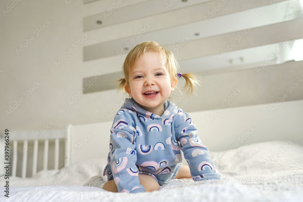 Adorable little smiling girl in beautiful suit at home on bed. Light and white interior. Adorable little smiling girl in beautiful suit at home on bed. Light and white interior.