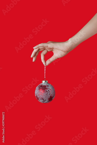 Elegant female hand holding a red snow-covered Christmas ball on a red background