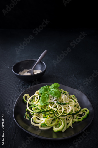 Zoodles, zucchini noodles with parmesan and basil on a black plate on black background. For low carb, keto, vegetarian, paleo nutrition and diet.  Vertical with copy space. photo