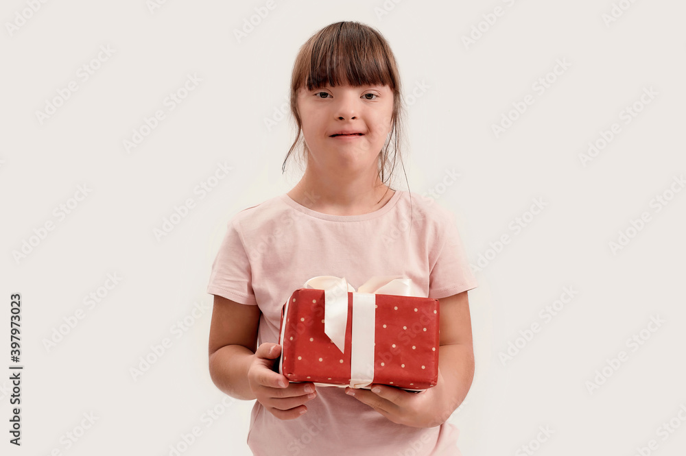 Portrait of disabled girl with Down syndrome smiling at camera, holding birthday present while posing isolated over white background Portrait of disabled girl with Down syndrome smiling at camera, holding birthday present while posing isolated over white background