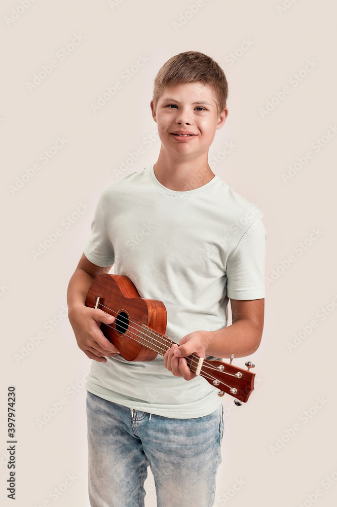 Fotografie Cheerful disabled boy with Down syndrome smiling at camera while playing ukulele