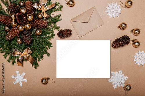 Christmas wreath decorations flat layout with space for text. Fir branches, pine cones, golden ornaments and craft envelope on the cardboard background. White sheet of paper in the center.