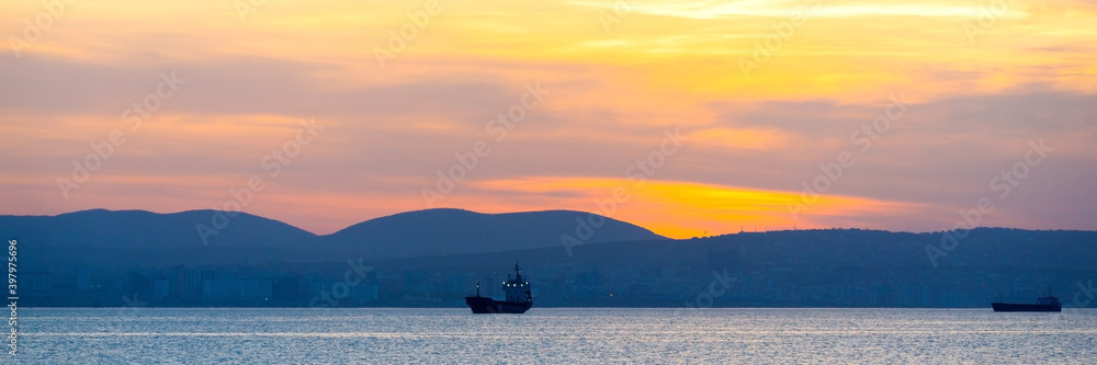 Golden sunset, silhouette of the city and cargo ship. Beautiful architecort by the sea on the background of the sunset - obrazy, fototapety, plakaty 