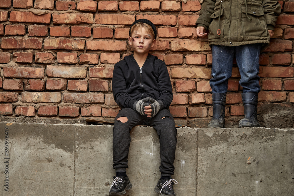 street kid boy sits on the concrete outdoors looking at camera, having no home, need shelter street kid boy sits on the concrete outdoors looking at camera, having no home, need shelter