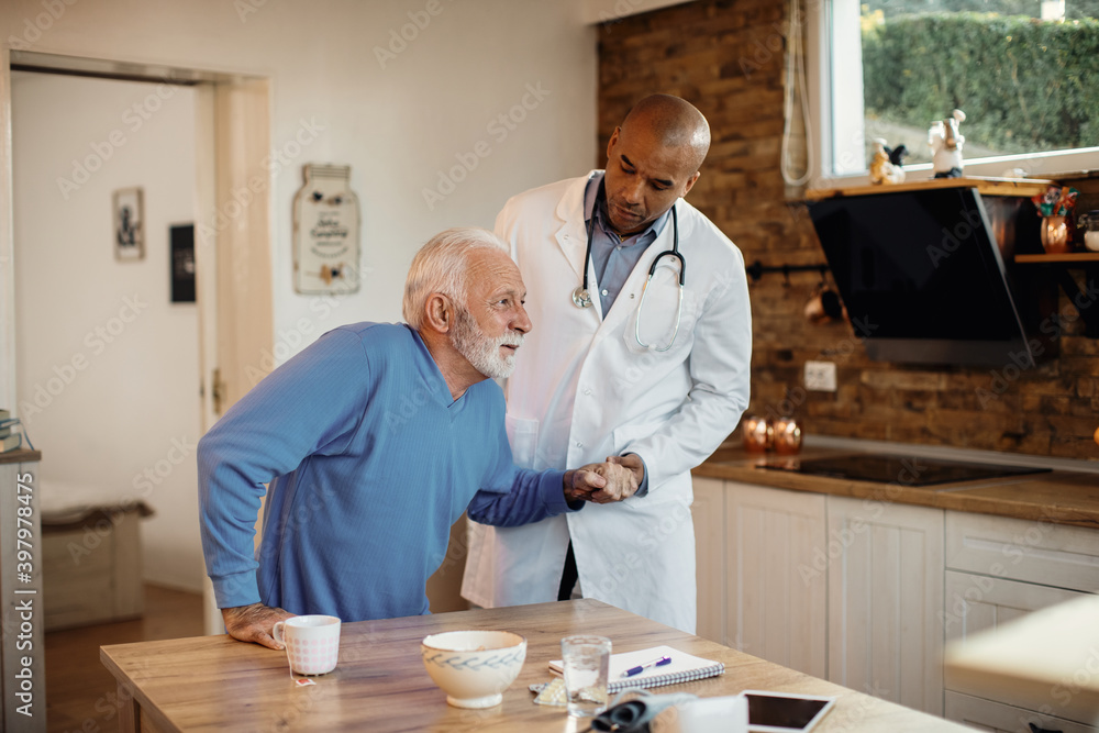 Φωτογραφία African American doctor helping senior man to get up from the chair during home visit