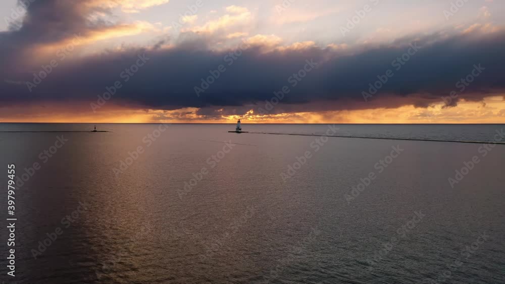 Beautiful sunset aerial hovering in front of the white colored Ludington breakwater lighthouse with blue and orange sky and clouds above reflecting on the calm tranquil water of Lake Michigan. Beautiful sunset aerial hovering in front of the white colored Ludington breakwater lighthouse with blue and orange sky and clouds above reflecting on the calm tranquil water of Lake Michigan.