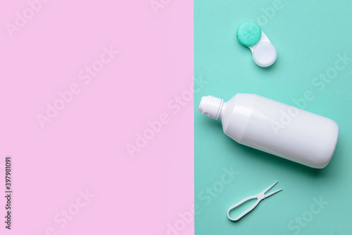 Container with contact lenses, solution and tweezers on color background