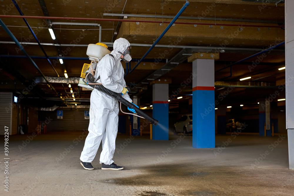 professional disinfecor in protective suit wearing face mask making disinfection outdoors of building, covid-19 concept