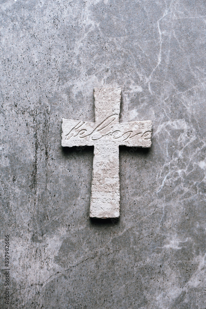 Stone cross with inscription Believe on grey background, Copy space. Christian backdrop. Biblical faith, gospel, salvation concept