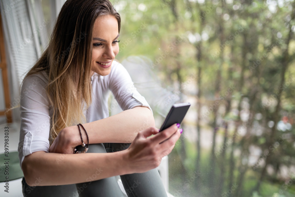 Fototapeta premium Beautiful young woman using her mobile phone at home.