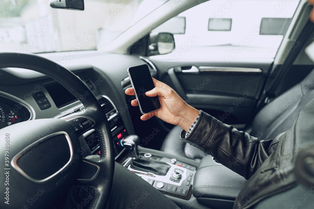 Male hand using smartphone while sitting in a car