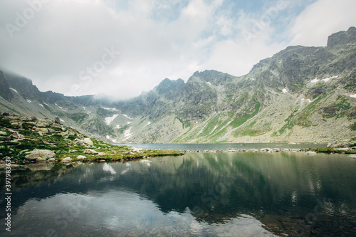 Picturesque landscape of crystal clear lake against the background of mountains in the fog.