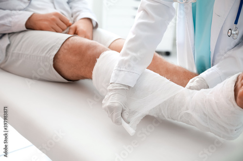 Doctor putting broken leg of young man in plaster