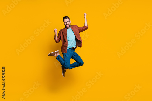Full length body size photo of male student jumping high gesturing like winner isolated on vibrant yellow color background