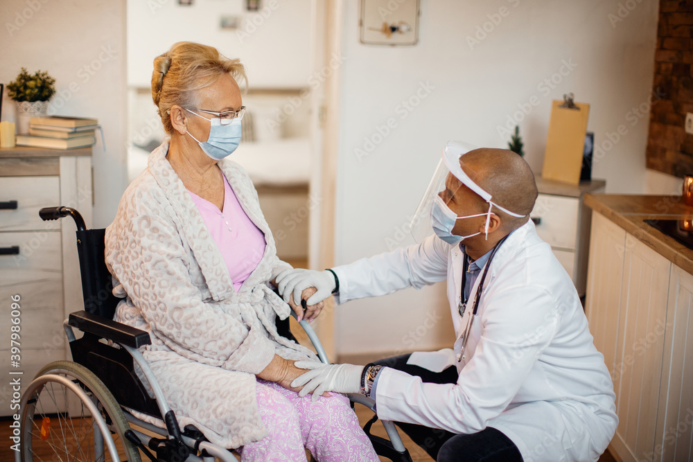 Caring doctor talking to senior woman in wheelchair at nursing home during coronavirus pandemic. Caring doctor talking to senior woman in wheelchair at nursing home during coronavirus pandemic.